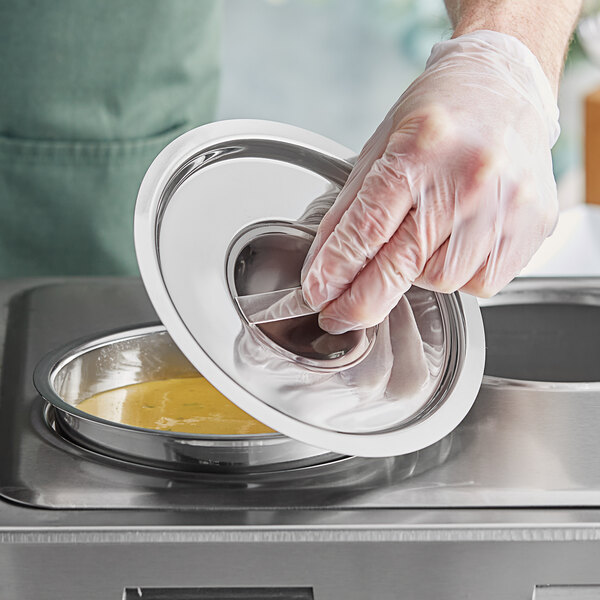 A gloved hand places a stainless steel lid on a metal container of food.