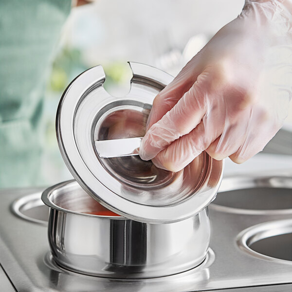 A person in a glove putting a Choice stainless steel vegetable inset cover on a pot.