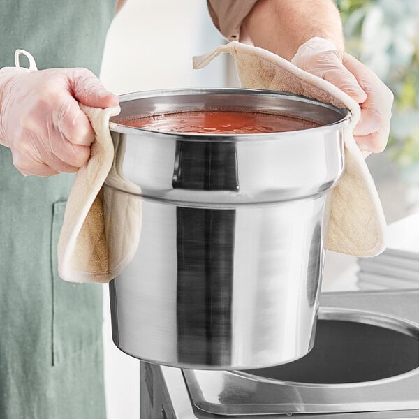 A person holding a Choice stainless steel vegetable inset over a pot of soup.