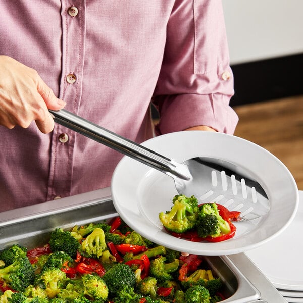 A person using a Choice stainless steel slotted basting spoon to serve vegetables on a plate.