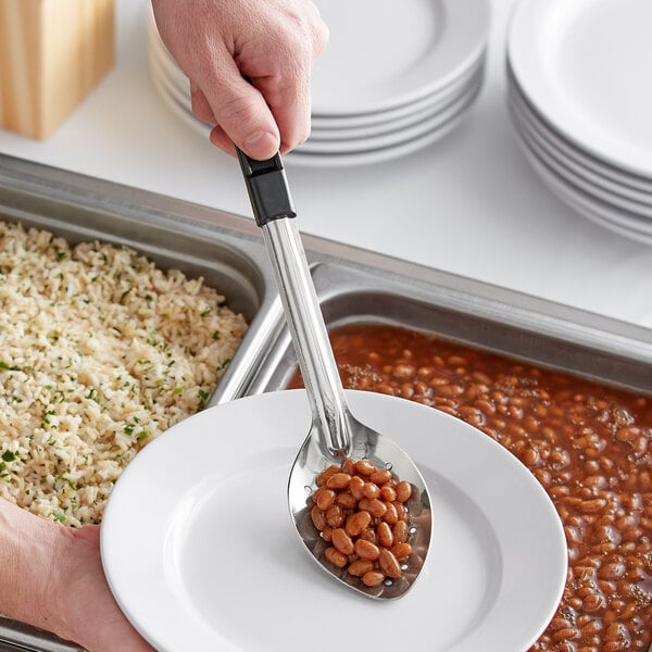 A person using a Choice perforated stainless steel basting spoon to serve beans onto a plate.