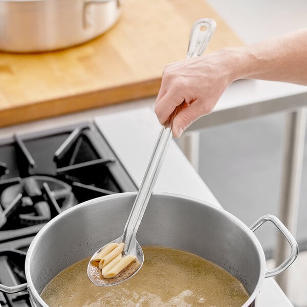 A Choice perforated stainless steel basting spoon stirring a pot of soup.