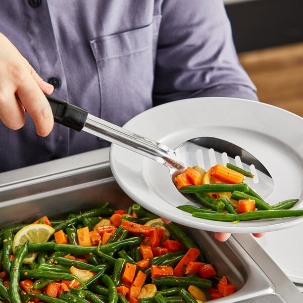 A person using a Choice slotted basting spoon to serve vegetables from a tray.