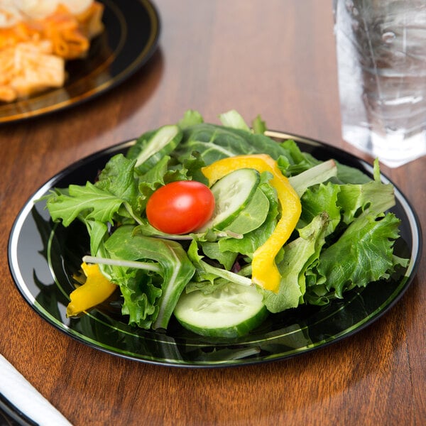 A Fineline Silver Splendor black plastic plate with a salad and a glass of water.