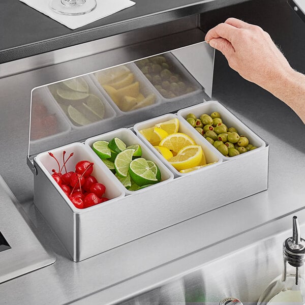 A Tablecraft stainless steel condiment bar with containers of fruit, vegetables, lemons, and olives.