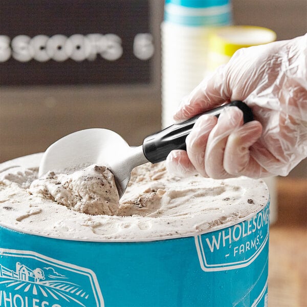 A gloved hand uses a Choice stainless steel ice cream spade to scoop ice cream into a blue container.