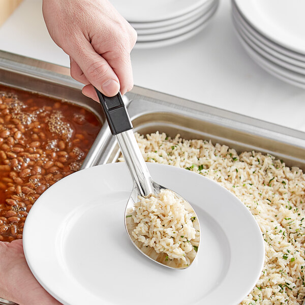 A person using a Choice stainless steel basting spoon with a black handle to serve rice onto a plate.