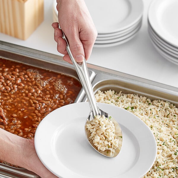 A person using a Choice stainless steel basting spoon to serve rice and beans on a plate.