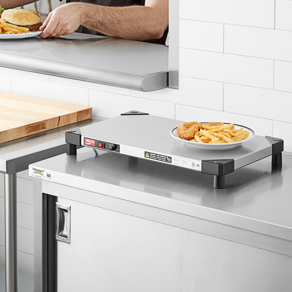 A man using a Metro stainless steel countertop shelf warmer to prepare a plate of chicken and french fries on a counter.