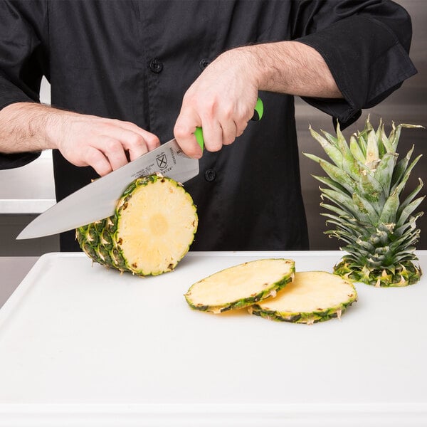 A person using a Mercer Culinary Millennia Colors chef knife to cut a pineapple.