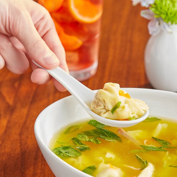 A hand holding a spoonful of food over a bowl with Acopa bright white ceramic Chinese soup spoon.