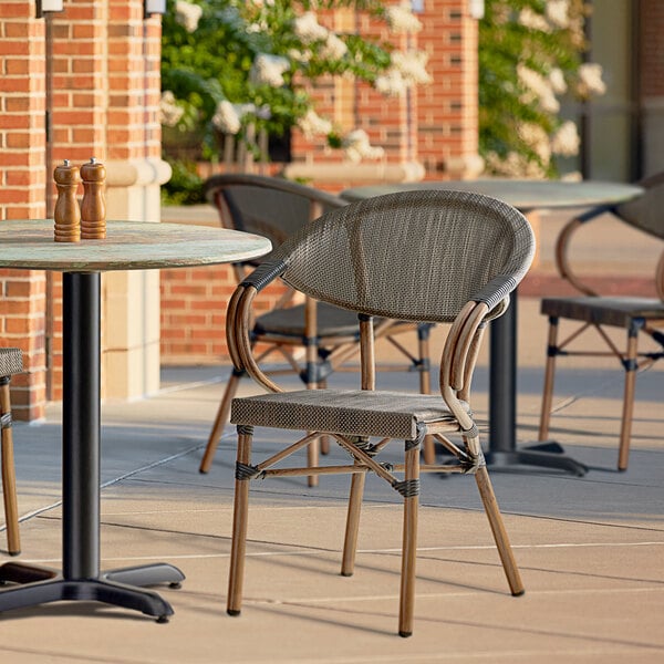 A brown Lancaster Table & Seating outdoor arm chair at a table on a patio.