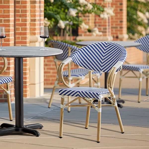 A blue and white striped Lancaster Table & Seating French Bistro outdoor arm chair on a patio.