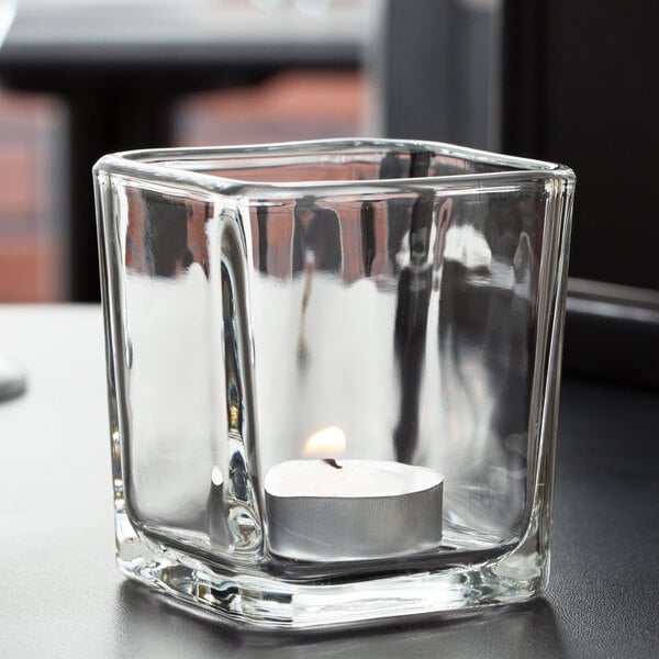 A Libbey glass cube candle holder with a lit candle inside.