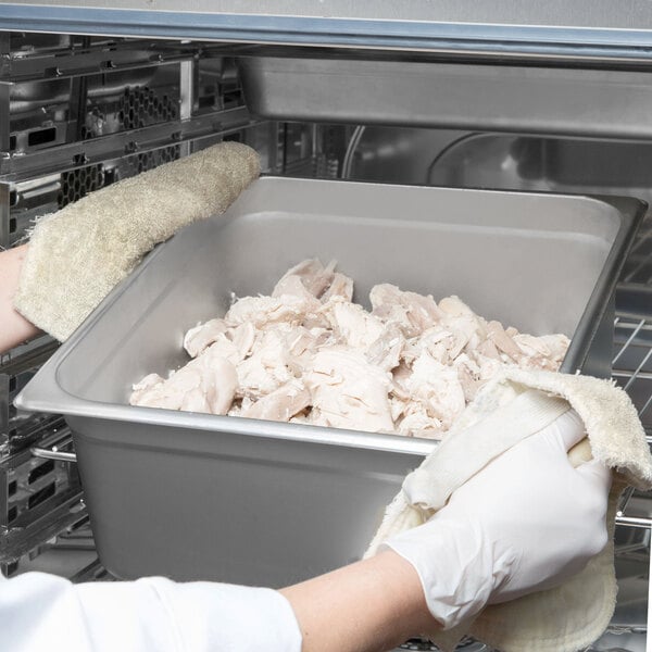 A person wearing gloves holding a Choice stainless steel steam table pan of meat.