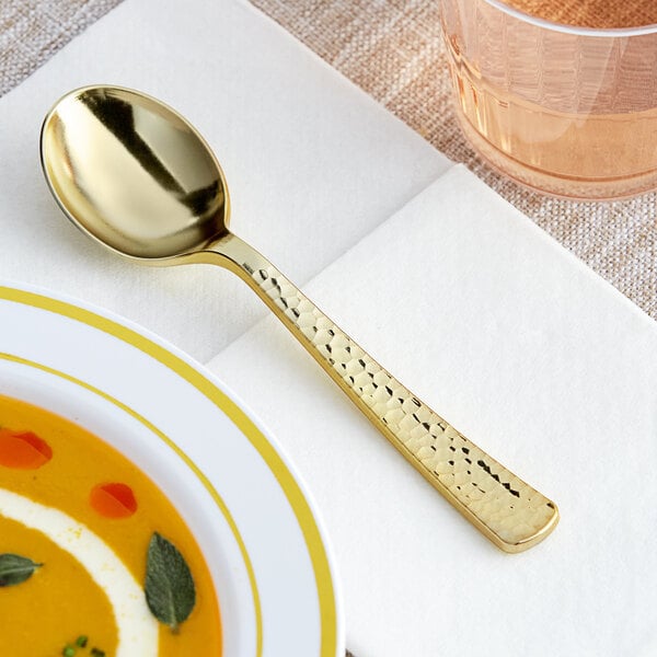 A Visions Hammersmith heavy weight gold plastic soup spoon on a plate.