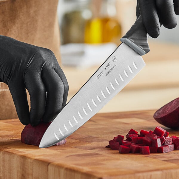 A person in black gloves uses a Schraf chef knife to cut a beet on a counter.