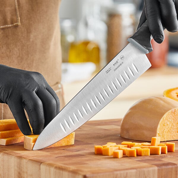 A person in black gloves using a Schraf chef knife to cut a carrot.