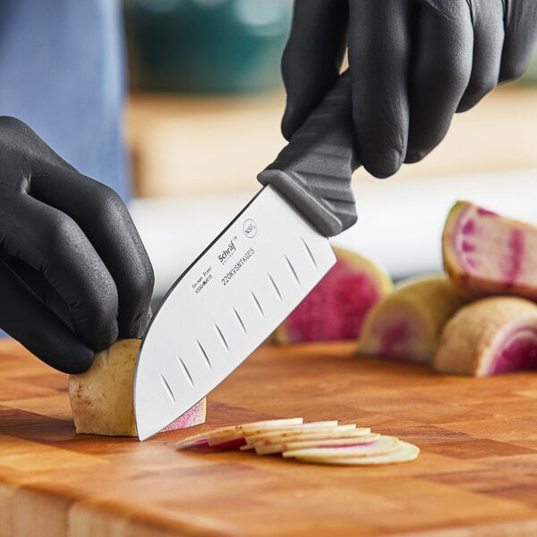 A person in black gloves using a Schraf Santoku knife with a TPRgrip handle to cut vegetables.