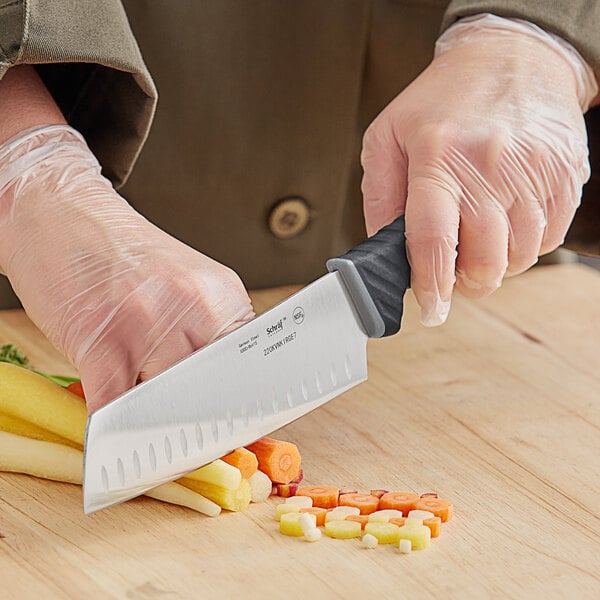 A person uses a Schraf Nakiri knife to cut vegetables on a counter.