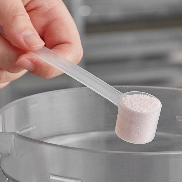A hand using a long-handled 7.5 cc polypropylene scoop to measure pink powder.