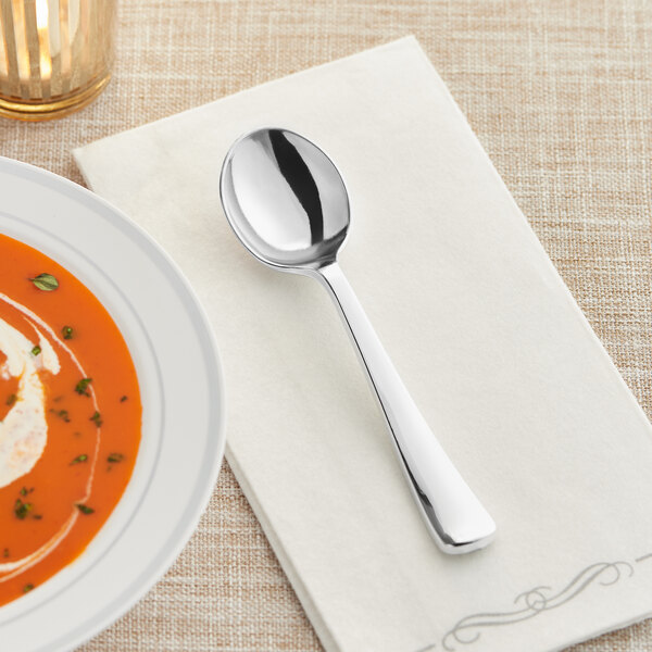A Visions heavy weight silver plastic soup spoon on a napkin next to a bowl of soup.