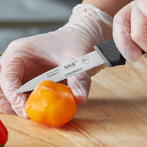 A person in gloves uses a Schraf serrated paring knife to cut a yellow bell pepper.