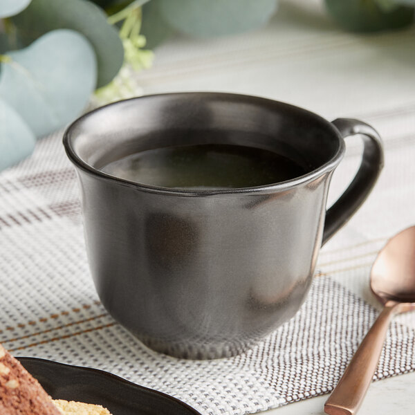 A matte gray Acopa Condesa scalloped porcelain cup filled with coffee on a table with a spoon.