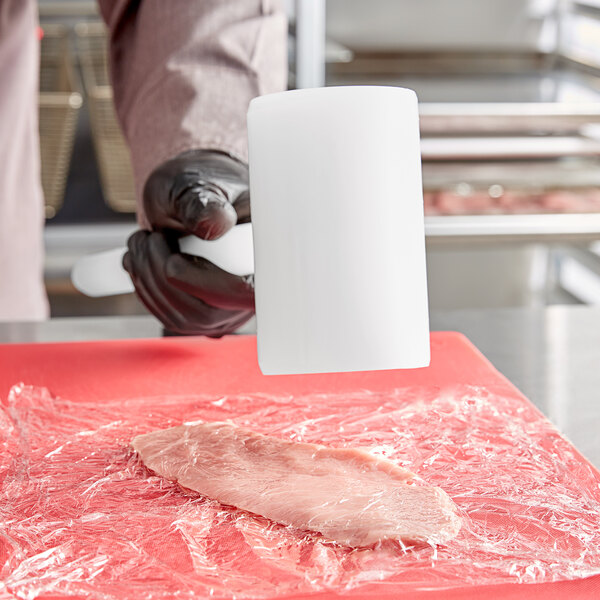 A person in gloves using an Omcan plastic meat tenderizer on a piece of meat.