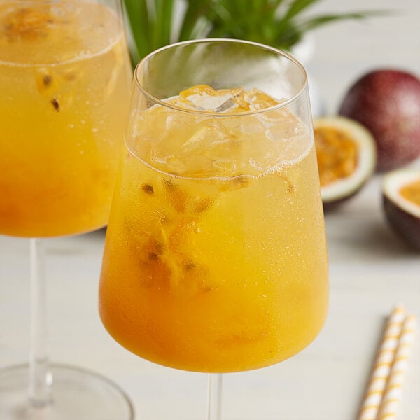A pair of glasses with passion fruit drinks and fruit on the side.