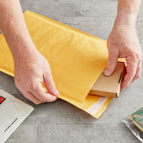 A person opening a brown Lavex Self-Sealing Kraft Bubble Mailer to reveal a book.