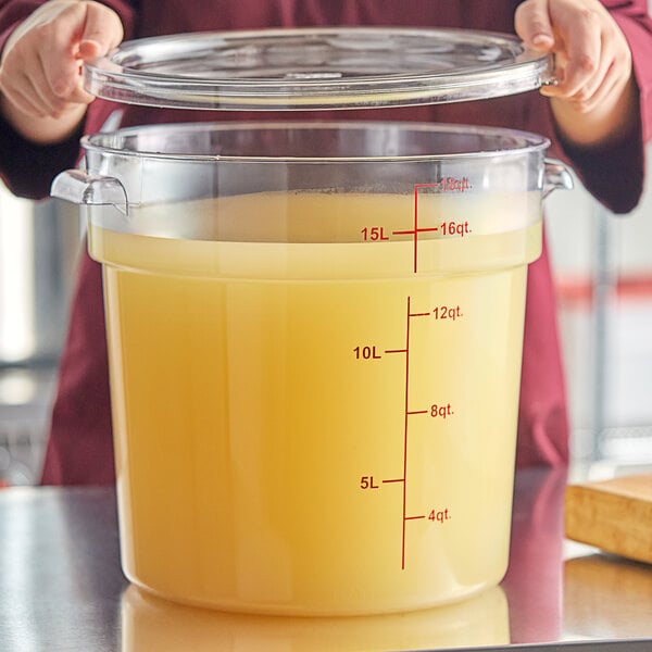 A woman using a measuring cup to pour yellow liquid into a large Choice clear container with a lid.