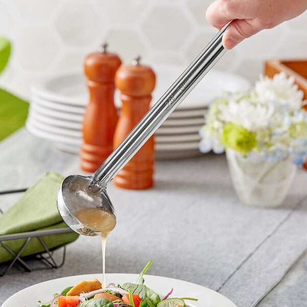 A person using a Choice stainless steel ladle to pour liquid onto a salad.