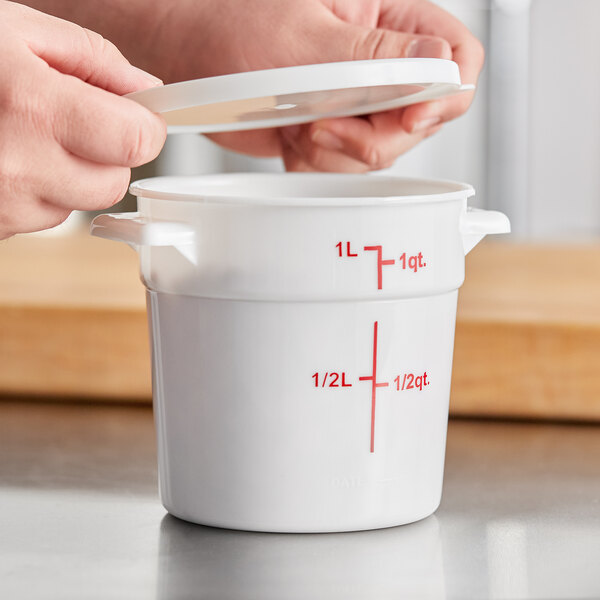 A person measuring out a Choice white round food storage container with a white measuring cup.