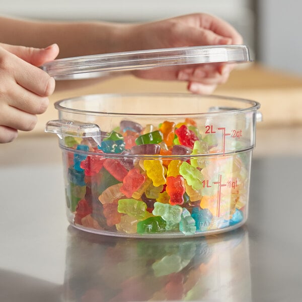 A person holding a clear plastic Choice food storage container filled with gummy bears.