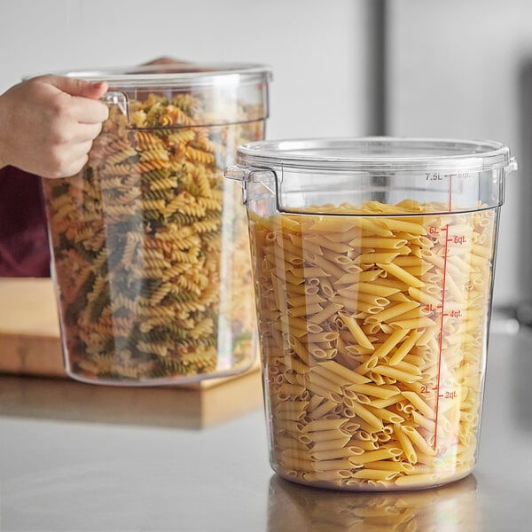 A hand holding a Choice clear polycarbonate food storage container full of pasta.
