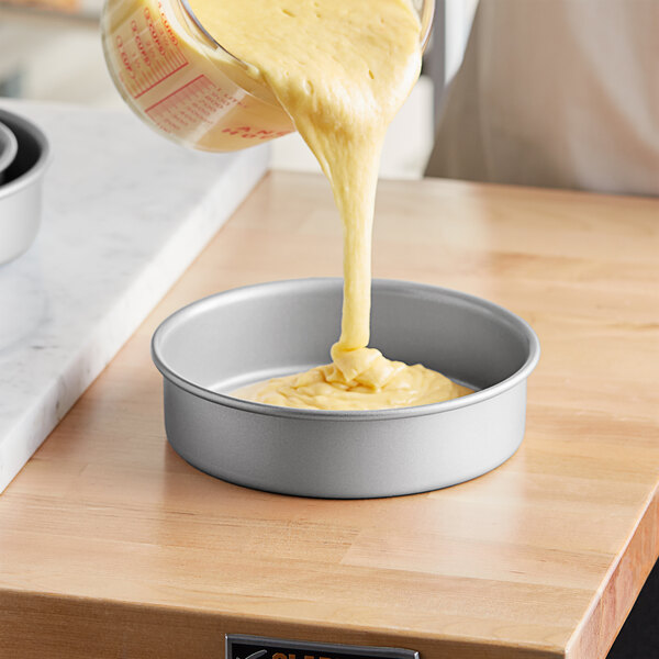 A person pouring yellow cake batter into a Baker's Mark round cake pan.