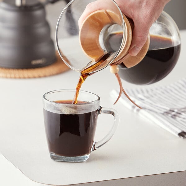 A person pouring Arrosto Brazil Santos Especial whole bean coffee into a glass cup.