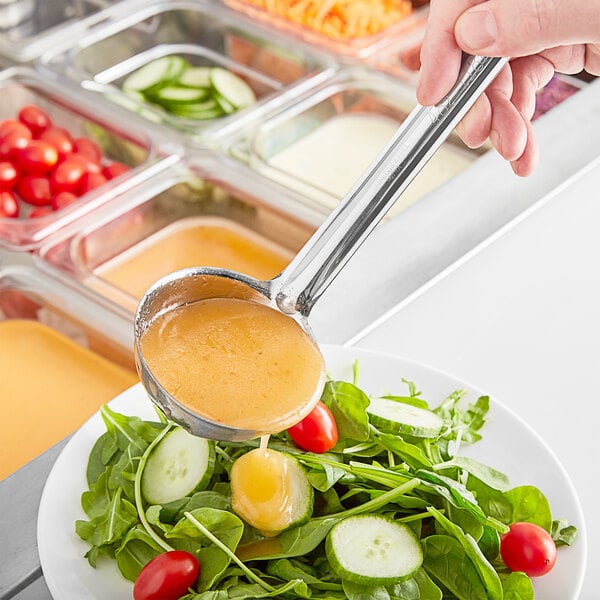 A person using a Choice stainless steel ladle to pour brown sauce over a bowl of salad.