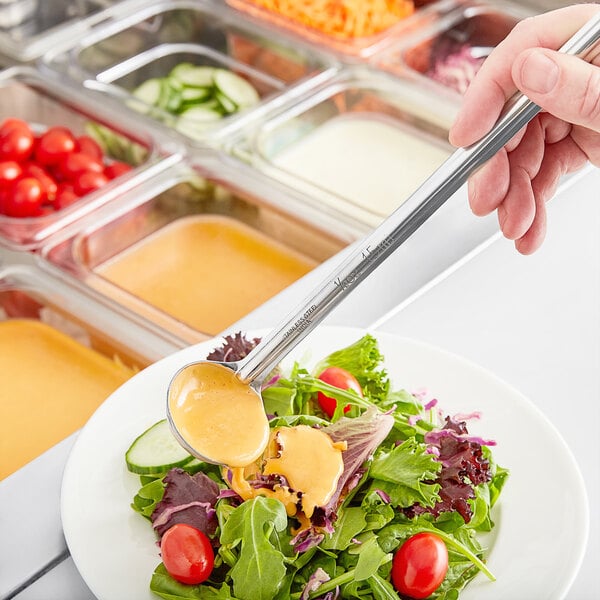 A hand holding a Choice stainless steel ladle over a plate of salad.