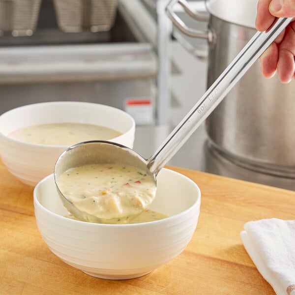 A person using a Choice stainless steel ladle to pour soup into a bowl.