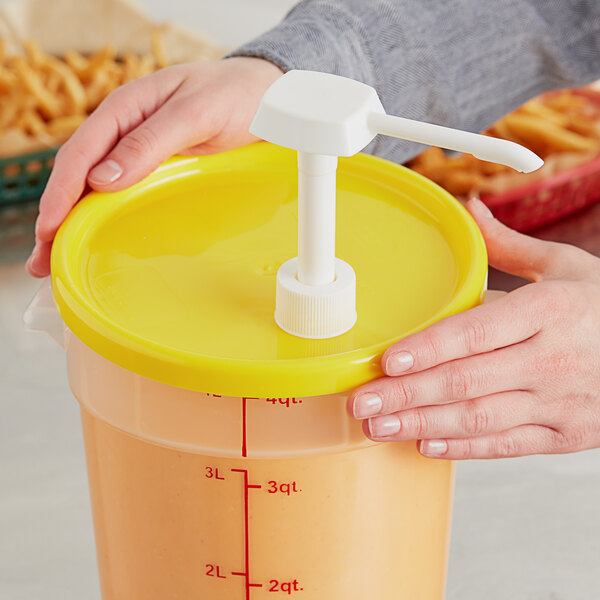 A person using a pump to pour fries into a container with a yellow lid.