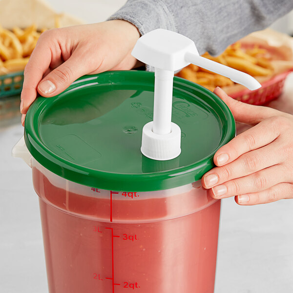 A hand holding a container with a green lid pouring liquid into another container.