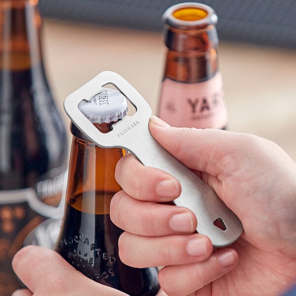 A person using a Franmara stainless steel bottle opener to open a bottle with a crown top.