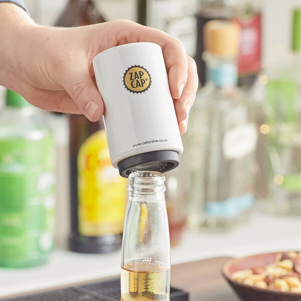 A hand using a Franmara Zap Cap bottle opener to pour a glass of beer.