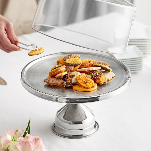A person holding a plate of cookies on a stainless steel stand.