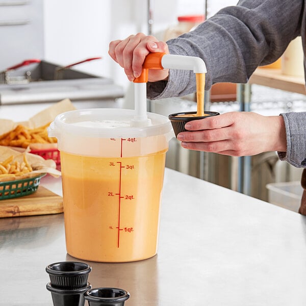 A person using a Choice Condiment Pump to pour orange liquid into a plastic container with a lid.