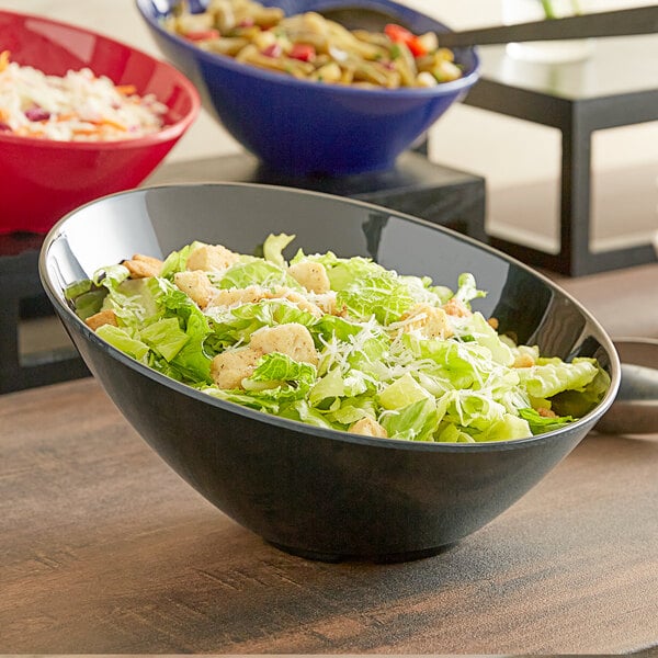 A black Acopa melamine bowl filled with salad on a table.