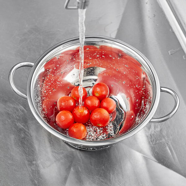 A stainless steel Choice colander filled with tomatoes under running water.