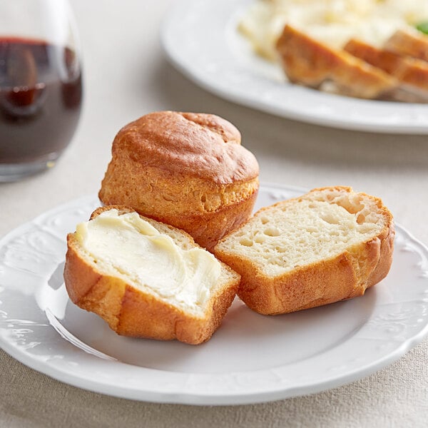 A plate with two Katz Gluten-Free Dinner Rolls with butter on top on a white background.